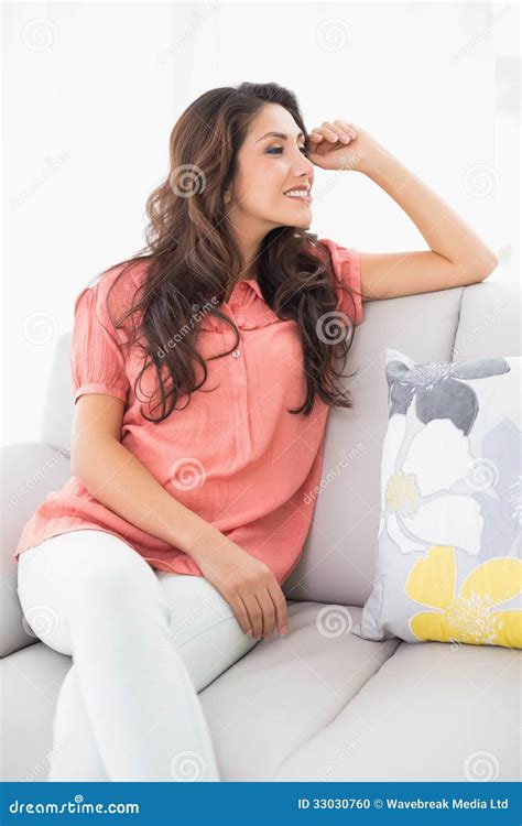 Smiling Brunette Sitting On Her Couch Looking Away Stock Photo Image