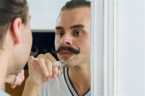 Reflexão no espelho de uma pessoa latina não binária consertando seu bigode uma tesoura