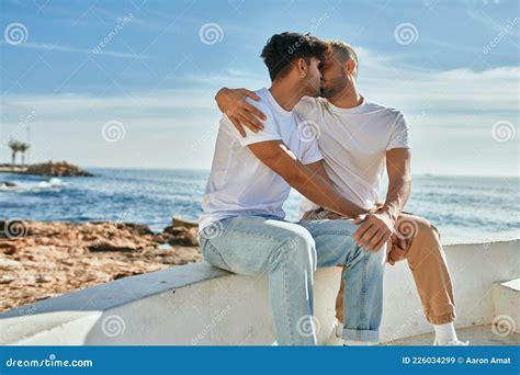 Jovem Casal Gay Sorrindo Feliz Sentado No Banco No Palco Da Praia Imagem De Stock Imagem De