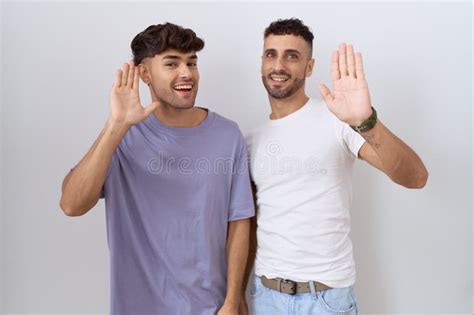 Homosexual Gay Couple Standing Over White Background Waiving Saying Hello Happy And Smiling