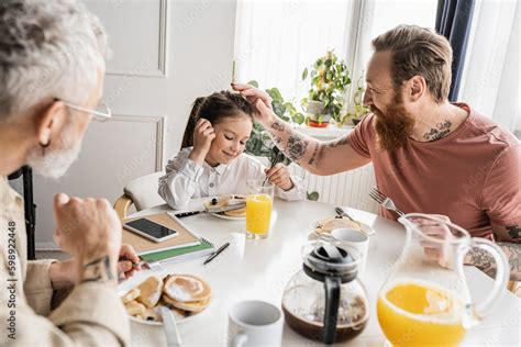 Cheerful Gay Dad Touching Head Of Preteen Girl Near Partner And Breakfast At Home Stock Photo