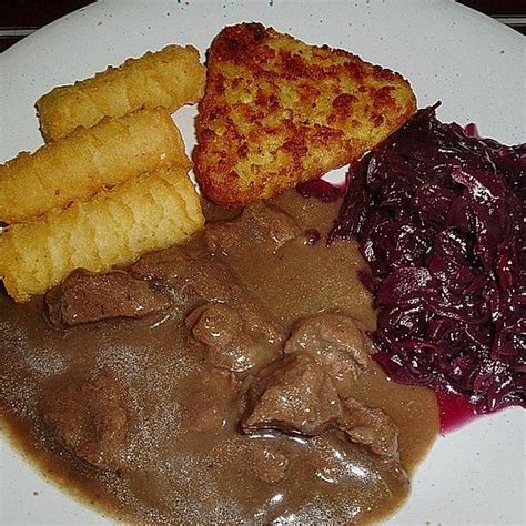 A White Plate Topped With Meat And Gravy Next To Fried Breadsticks