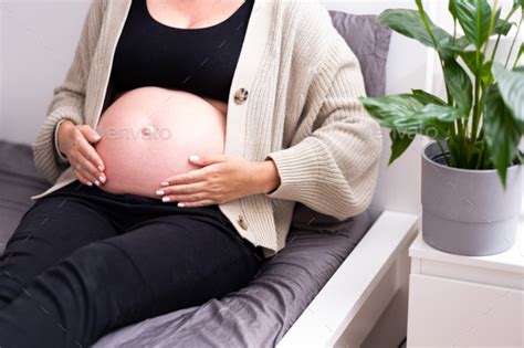 Unrecognizable Pregnant Woman Lying On Bed Caressing Naked Baby Bump Belly Indoors At Home