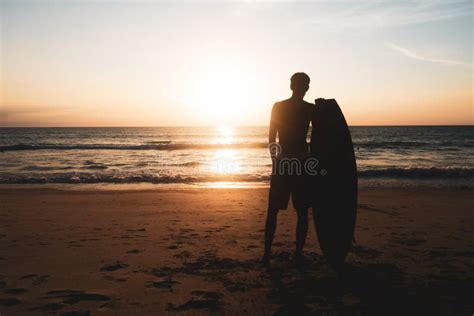 Silhouette Of Surfer Man Carrying Their Surfboards On Sunset Beach With