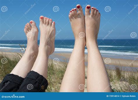 Piernas De Dos Mujeres Que Toman El Sol En La Playa Foto De Archivo