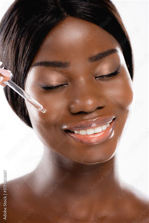 Naked African American Woman With Closed Eyes Applying Serum On Face Isolated On White Stock