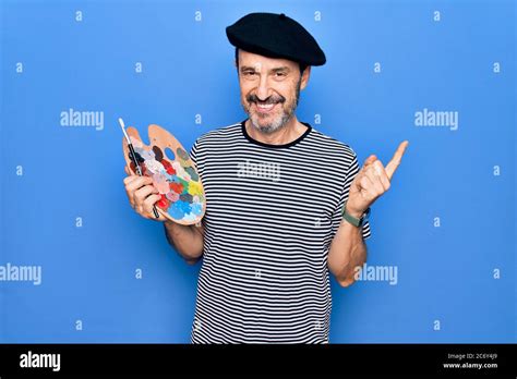 Middle age handsome artist man wearing french beret drawing using paintbrush and palette smiling ...
