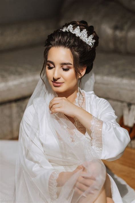 The Brunette Bride Dressed In A Satin Robe Sits On The Couch Beautiful Hair And Makeup Stock