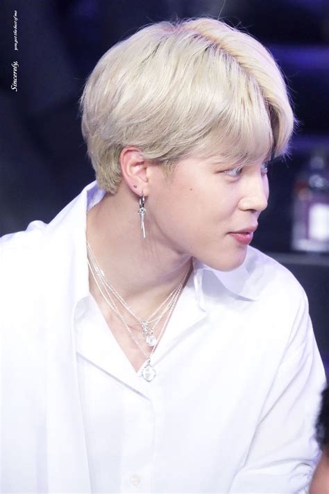 A Woman With Blonde Hair Wearing A White Shirt And Silver Earrings