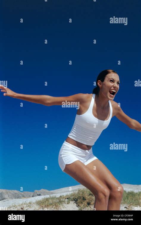 Female Brunette Hair Off Face Wearing White Vest Top And White Hot Pants Standing Arms Out To