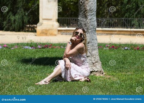 Jovem Loira E Latina Sentada Na Sombra Ao Lado Do Tronco De Uma Palmeira No Parque Fazendo