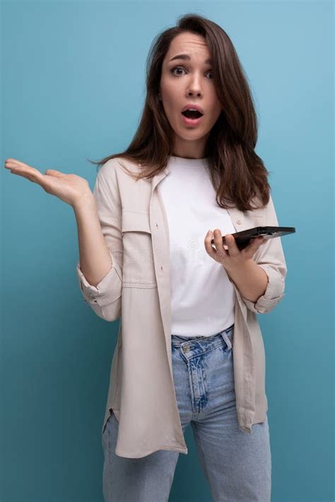 Surprised Adorable Brunette 30 Year Old Female Person In Shirt And Jeans With Smartphone Stock
