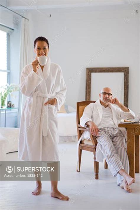 Mature Woman Drinking A Cup Of Coffee And Smiling With A Mature Woman Sitting Behind Her