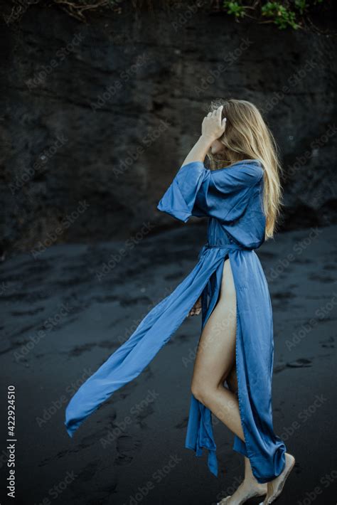 Photoshoot Of A Blonde Girl In A Blue Dress On The Bali Beach With Black Sand Stock Photo