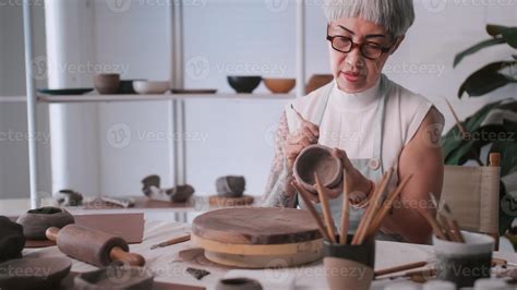 Asian elderly woman enjoying pottery work at home. A female ceramicist ...