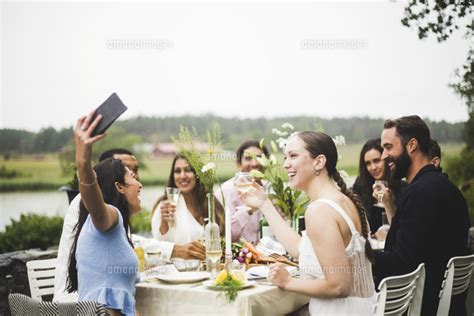 Cheerful Young Woman Taking Selfie With Friends During Dinner Party In