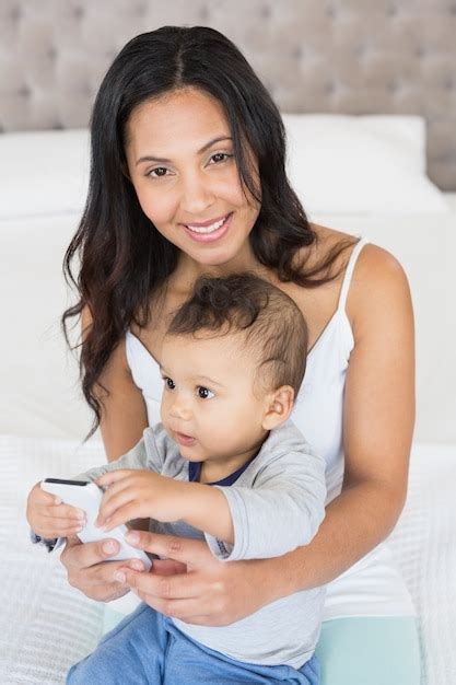 Premium Photo Happy Brunette Holding Her Baby And Using Smartphone In Bedroom