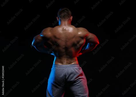 Male Bodybuilder Athlete With Naked Torso Posing Against A Black Background In Red And Blue