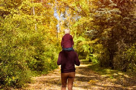 Padre con hijo sobre sus hombros caminando en el bosque de otoño vista