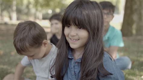 Vídeo Gratis Encantadora chica latina sentada en el césped en el parque con amigos