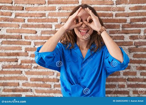 Beautiful Brunette Woman Standing Over Bricks Wall Doing Ok Gesture Like Binoculars Sticking