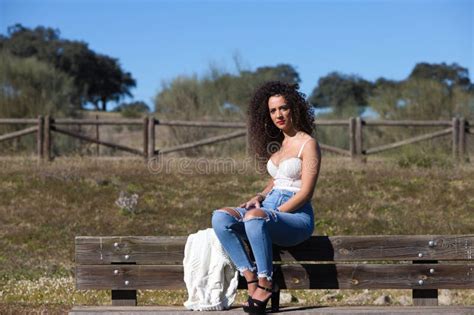 Spanish Brunette Curly Haired Woman Sits On A Bench On The Path Leading To The Forest She Is