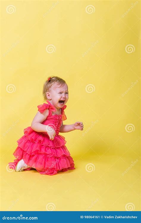 Little Girl In Pink Dress Kneeling And Crying On A Yellow Background