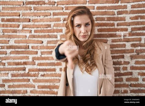 Belle femme blonde debout sur le mur de briques regardant malheureux et en colère montrant le