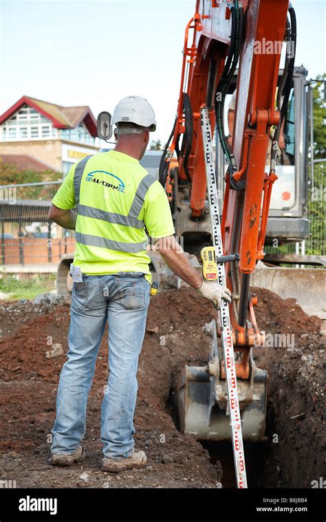 Workman Measures The Depth Of A Trench Dug By A Jcb Stock Photo Alamy