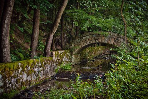 Stone Arch Bridge Path And Flowing Creek Stream In Lush Forest