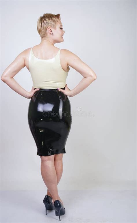 Hot Short Hair Blonde Girl With Curvy Body Wearing Latex Rubber Dress On White Studio Background