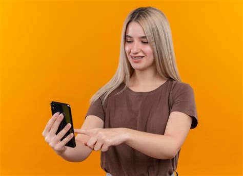 Souriante Jeune Fille Blonde Dans Un Appareil Dentaire Tenant Un Téléphone Mobile Et Le Toucher