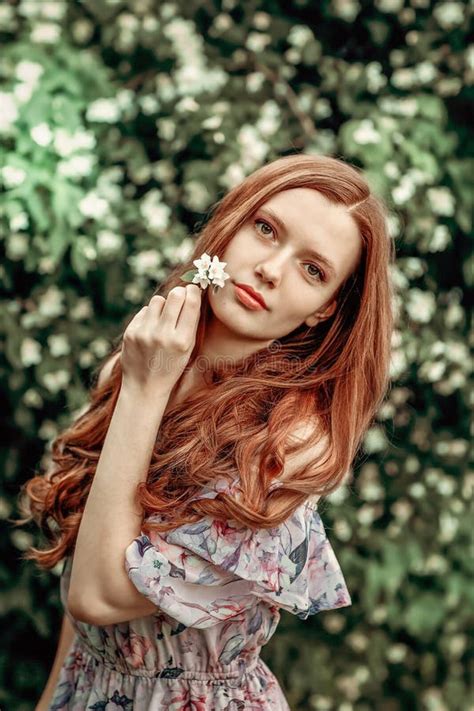 A Girl In A Light Summer Dress Stands Near A Bird Cherry Bush On A Hot Summer Day Stock Photo