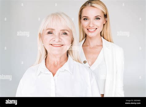 Smiling Blonde Grandmother And Granddaughter Together In Total White Outfits Isolated On Grey