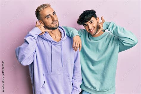Homosexual Gay Couple Standing Together Wearing Casual Clothes Smiling Doing Phone Gesture With