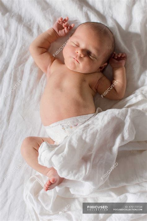 Новорожденный ребенок спит на белой кровати с белыми простынями ...
