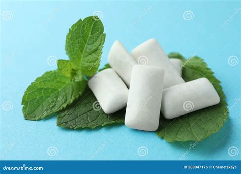 Tasty White Chewing Gums And Mint Leaves On Light Blue Background