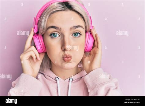 Jeune fille blonde écoutant de la musique en utilisant des écouteurs puffant les joues avec le