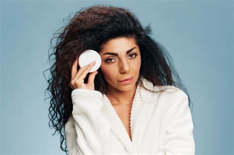 Mujer latina bastante rizada en bata de baño sonriendo sostenga el tarro de crema en la mejilla