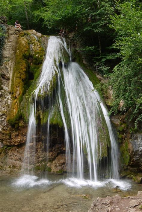 Muchacha Que Se Sienta En El Top De Un Goteo De La Cascada En Las Rocas