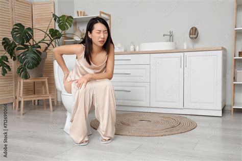 Young Asian Woman With Hemorrhoids Sitting On Toilet Bowl In Restroom