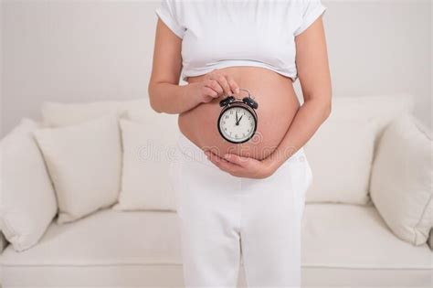A Pregnant Woman With A Naked Belly Holds An Alarm Clock Intended Date Of Birth Stock Image