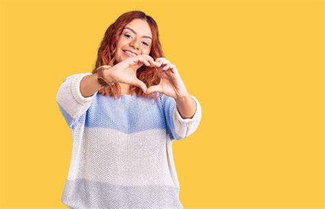 Jovem latina vestindo roupas casuais sorrindo apaixonadamente fazendo forma de símbolo de
