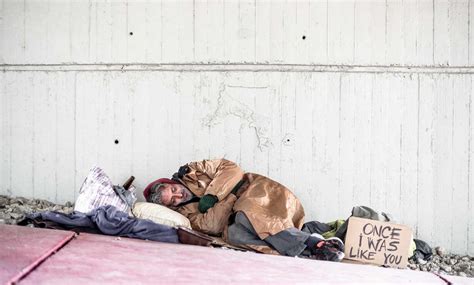 A Homeless Beggar Man Lying On The Ground Outdoors In City Sleeping