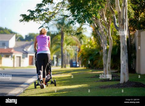 Back View Of Young Mother Pushing Baby In Stroller Along Urban Street