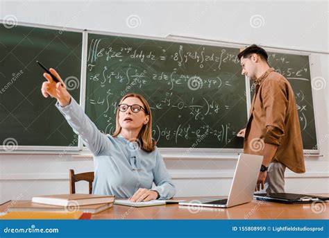 Female Teacher Sitting At Desk And Pointing At Something Stock Image