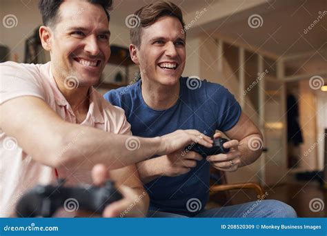Loving Same Sex Male Couple Sitting On Sofa At Home Gaming Together Stock Image Image Of Gamer