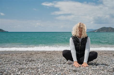 Une femme européenne blonde est assise sur une plage de galets un jour de printemps touche les