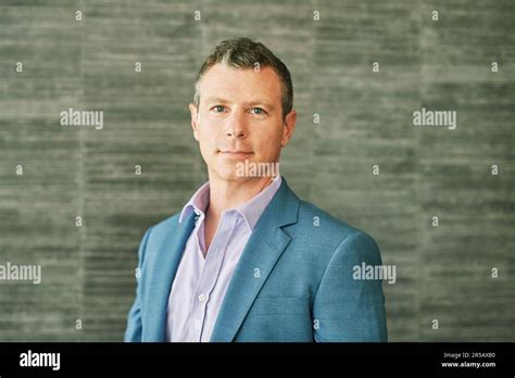 Portrait Of Mature 40 Year Old Man Posing Bext To Grey Wall Background Wearing Purple Shirt And