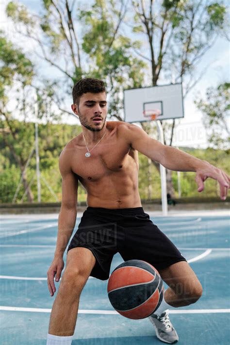 Concentrated Male Athlete With Naked Torso Playing Basketball Alone On Sports Ground In Summer